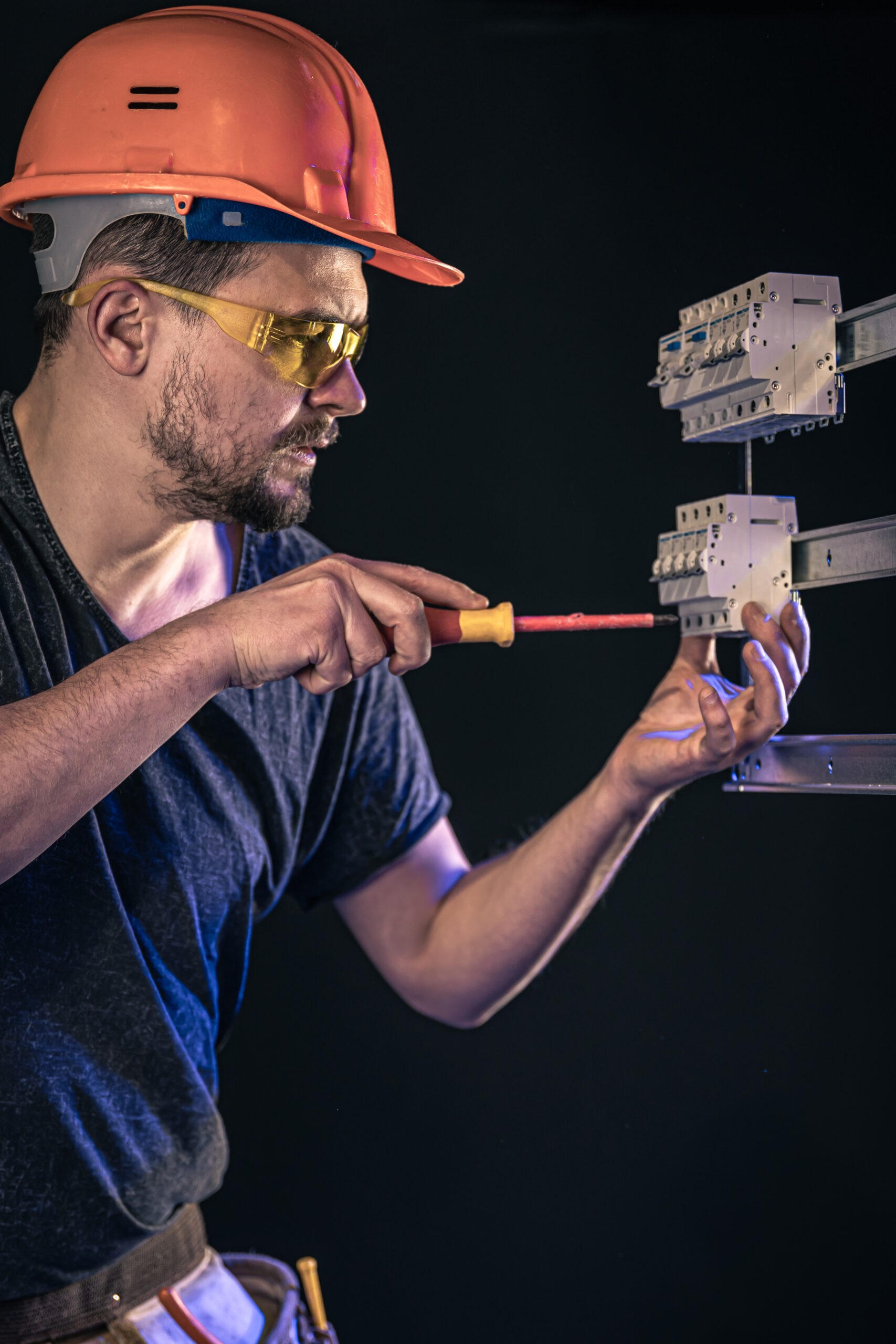 A male electrician works in a switchboard with an electrical connecting cable.